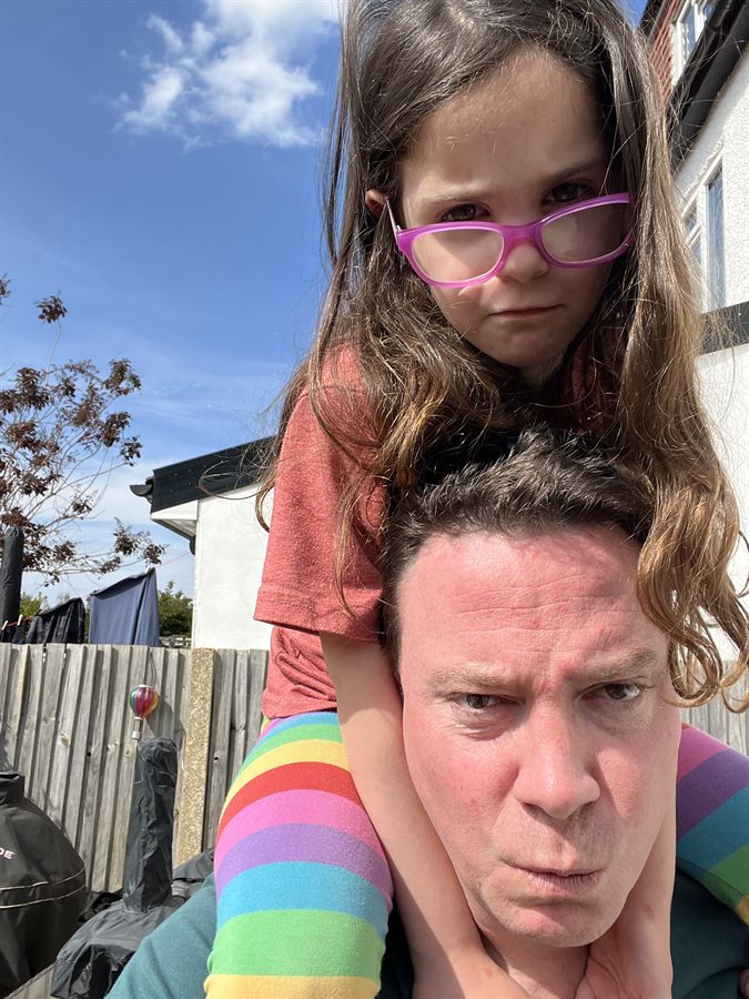Richard with his daughter on his shoulders, both thoroughly unimpressed, under a clear blue sky